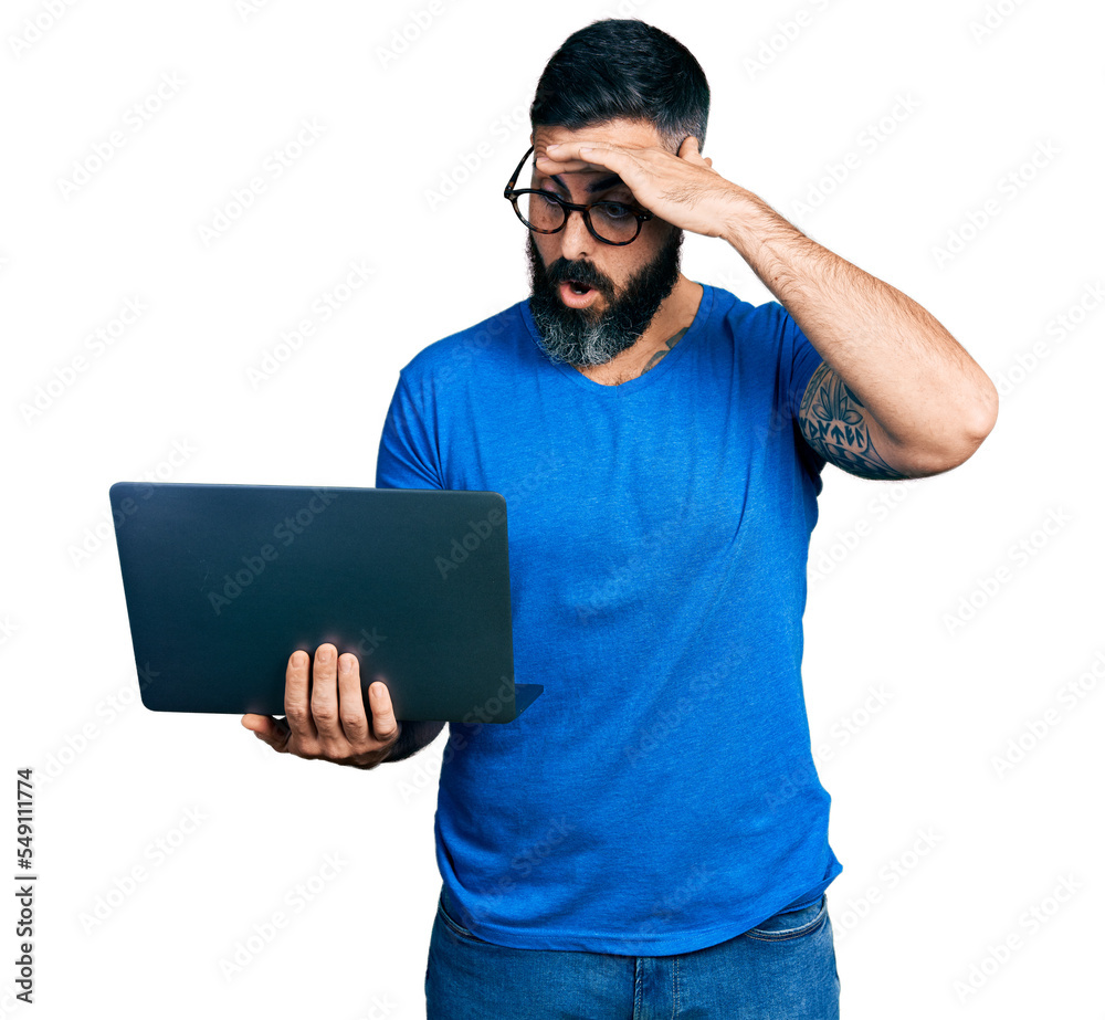 Hispanic man with beard working using computer laptop stressed and frustrated with hand on head, surprised and angry face Hispanic man with beard working using computer laptop stressed and frustrated with hand on head, surprised and angry face