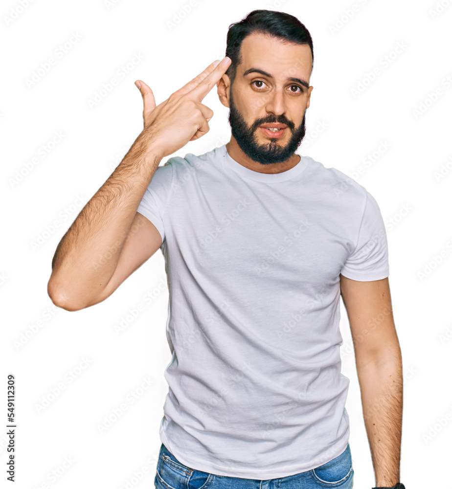 Young man with beard wearing casual white t shirt shooting and killing oneself pointing hand and fingers to head like gun, suicide gesture. Young man with beard wearing casual white t shirt shooting and killing oneself pointing hand and fingers to head like gun, suicide gesture.