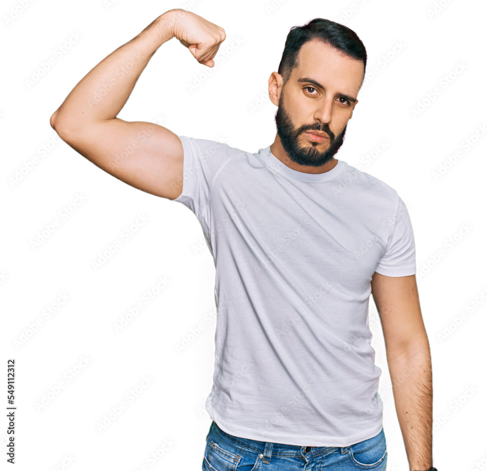 Young man with beard wearing casual white t shirt strong person showing arm muscle, confident and proud of power Young man with beard wearing casual white t shirt strong person showing arm muscle, confident and proud of power
