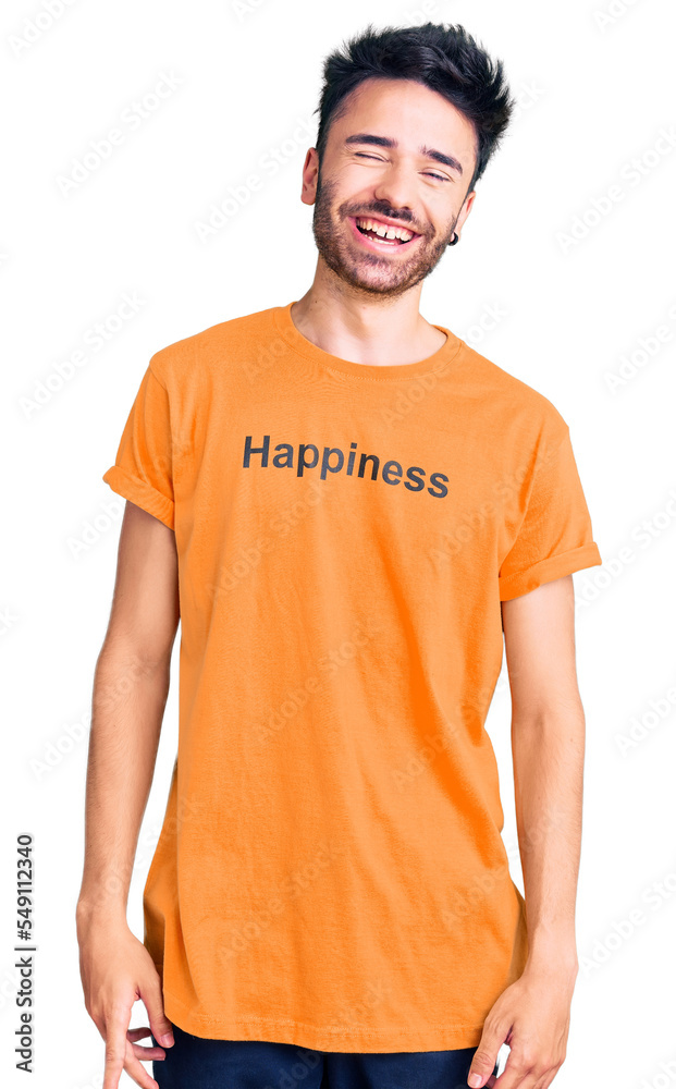 Young hispanic man wearing t shirt with happiness word message winking looking at the camera with sexy expression, cheerful and happy face. Young hispanic man wearing t shirt with happiness word message winking looking at the camera with sexy expression, cheerful and happy face.