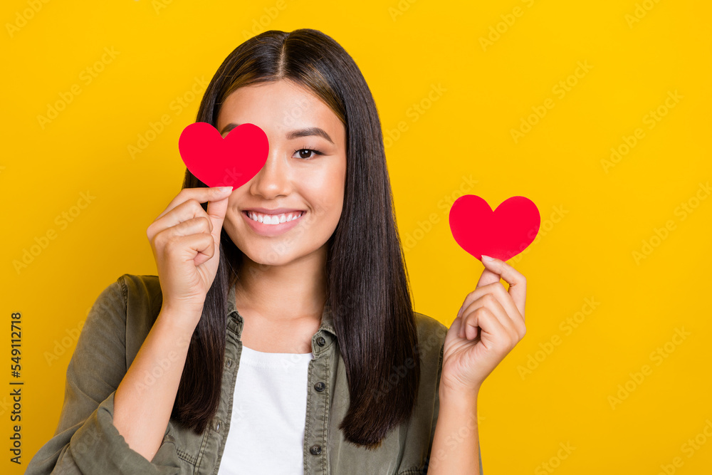 Portrait of charming glad japanese confident woman cover eye red paper heart love want date new boyfriend isolated on yellow color background Portrait of charming glad japanese confident woman cover eye red paper heart love want date new boyfriend isolated on yellow color background