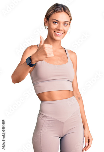 Beautiful caucasian woman wearing sportswear doing happy thumbs up gesture with hand. approving expression looking at the camera showing success.