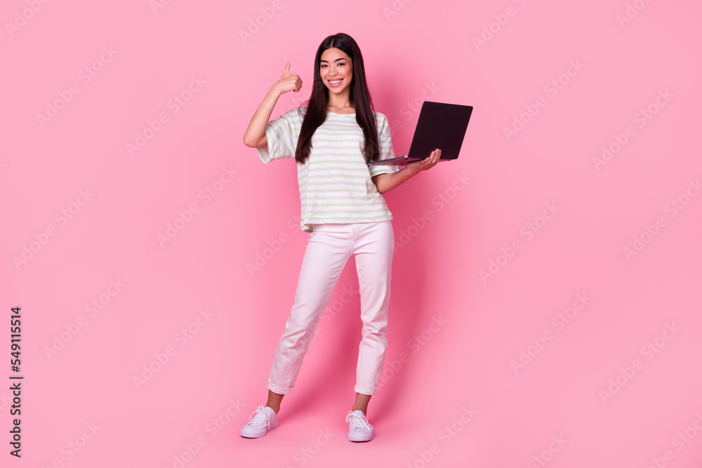 Full body portrait of cheerful attractive malaysian lady demonstrate thumb up hold laptop isolated on pink color background Full body portrait of cheerful attractive malaysian lady demonstrate thumb up hold laptop isolated on pink color background