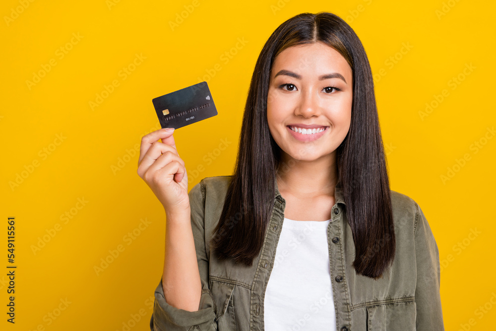 Photo of toothy beaming girl with brunette hair wear gray shirt hold debit card wireless payment isolated on yellow color background Photo of toothy beaming girl with brunette hair wear gray shirt hold debit card wireless payment isolated on yellow color background