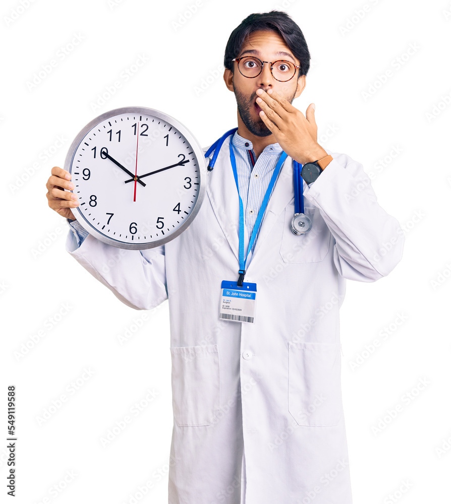 Handsome hispanic man wearing doctor uniform holding clock covering mouth with hand, shocked and afraid for mistake. surprised expression Handsome hispanic man wearing doctor uniform holding clock covering mouth with hand, shocked and afraid for mistake. surprised expression