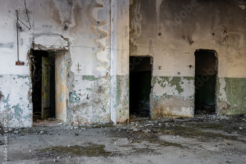 View of a wall with empty doorways in an abandoned room. Peeling paint on cracked walls. Deserted ruins in an abandoned ghost town. Garbage on dirty concrete floor. Gloomy background for design.