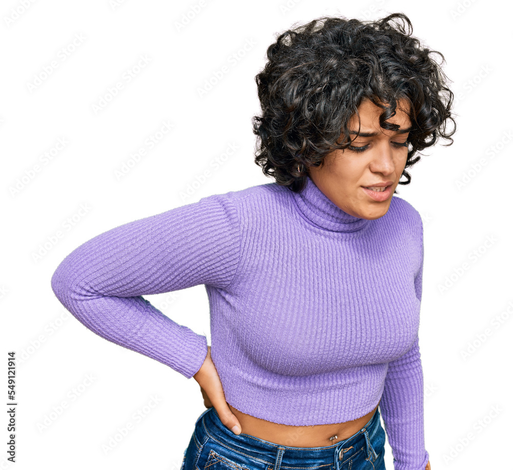 Young hispanic woman with curly hair wearing casual clothes suffering of backache, touching back with hand, muscular pain Young hispanic woman with curly hair wearing casual clothes suffering of backache, touching back with hand, muscular pain
