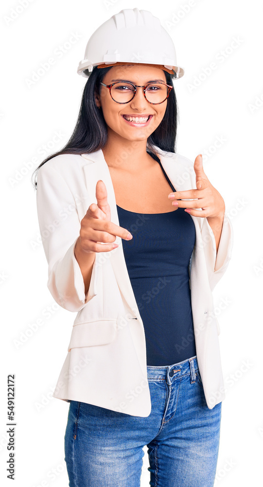Young beautiful latin girl wearing architect hardhat and glasses pointing fingers to camera with happy and funny face. good energy and vibes. Young beautiful latin girl wearing architect hardhat and glasses pointing fingers to camera with happy and funny face. good energy and vibes.