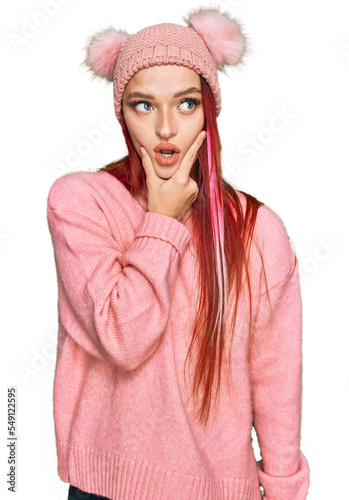 Young caucasian woman wearing casual clothes and wool cap looking fascinated with disbelief, surprise and amazed expression with hands on chin
