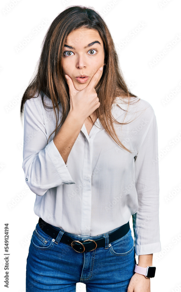 Young caucasian girl wearing casual white shirt looking fascinated with disbelief, surprise and amazed expression with hands on chin Young caucasian girl wearing casual white shirt looking fascinated with disbelief, surprise and amazed expression with hands on chin