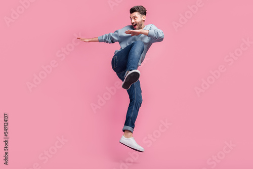 Full body size photo of young handsome attractive funny man student wear casual clothes look empty space jump ninja fight isolated on pink color background