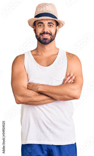Young hispanic man wearing casual summer hat happy face smiling with crossed arms looking at the camera. positive person.