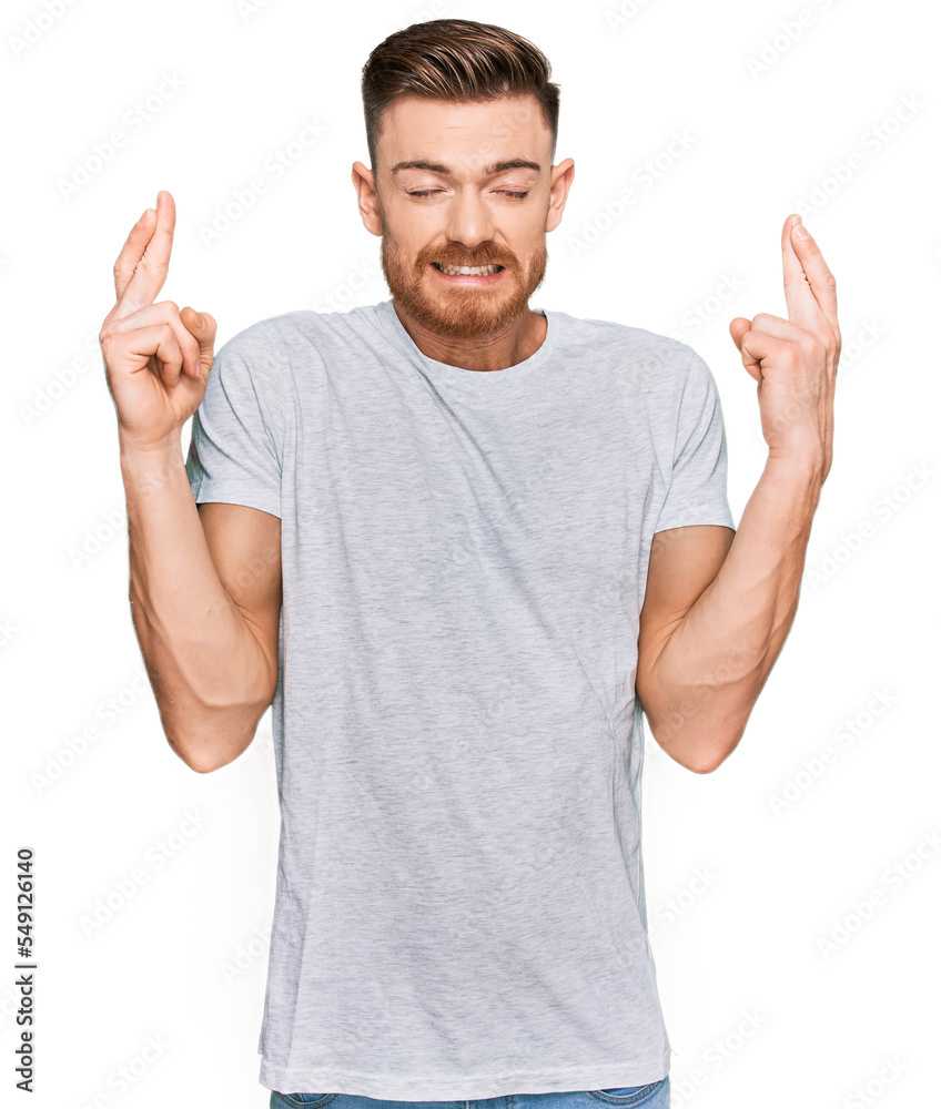 Fototapeta premium Young redhead man wearing casual grey t shirt gesturing finger crossed smiling with hope and eyes closed. luck and superstitious concept.