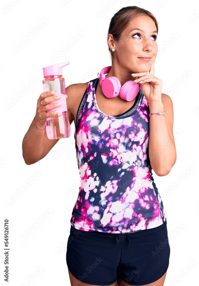 Young beautiful hispanic woman wearing sportswear holding water bottle serious face thinking about question with hand on chin, thoughtful about confusing idea