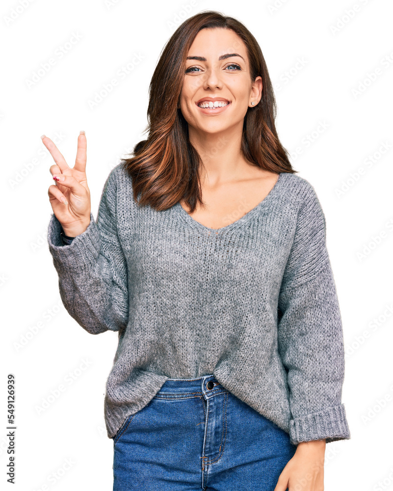 Young brunette woman wearing casual winter sweater smiling with happy face winking at the camera doing victory sign. number two. Young brunette woman wearing casual winter sweater smiling with happy face winking at the camera doing victory sign. number two.