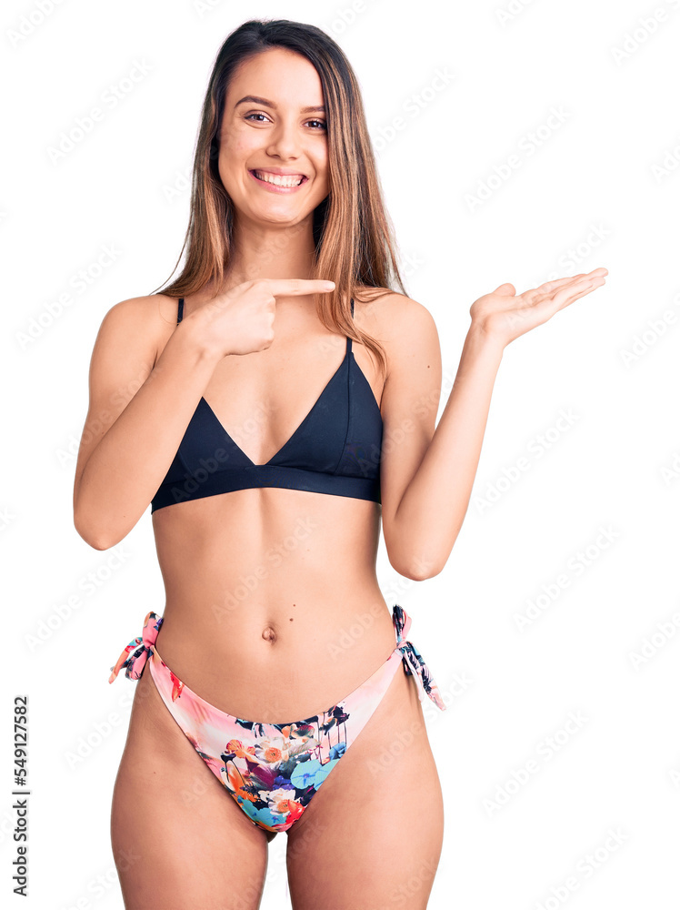 Young beautiful girl wearing bikini amazed and smiling to the camera while presenting with hand and pointing with finger.