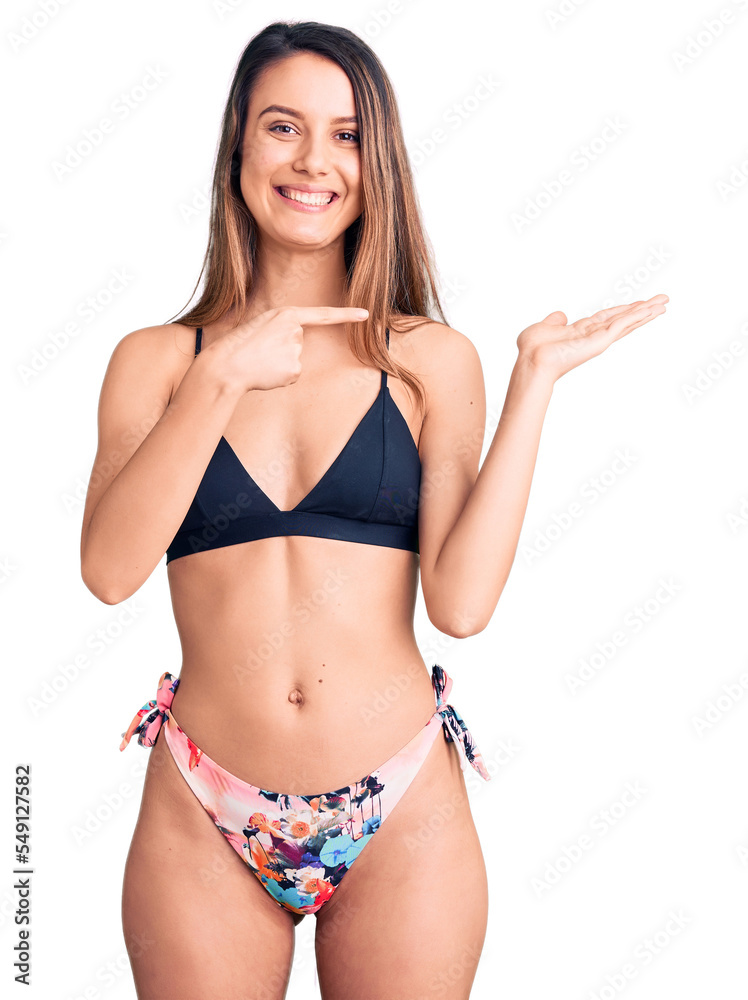 Young beautiful girl wearing bikini amazed and smiling to the camera while presenting with hand and pointing with finger. Young beautiful girl wearing bikini amazed and smiling to the camera while presenting with hand and pointing with finger.
