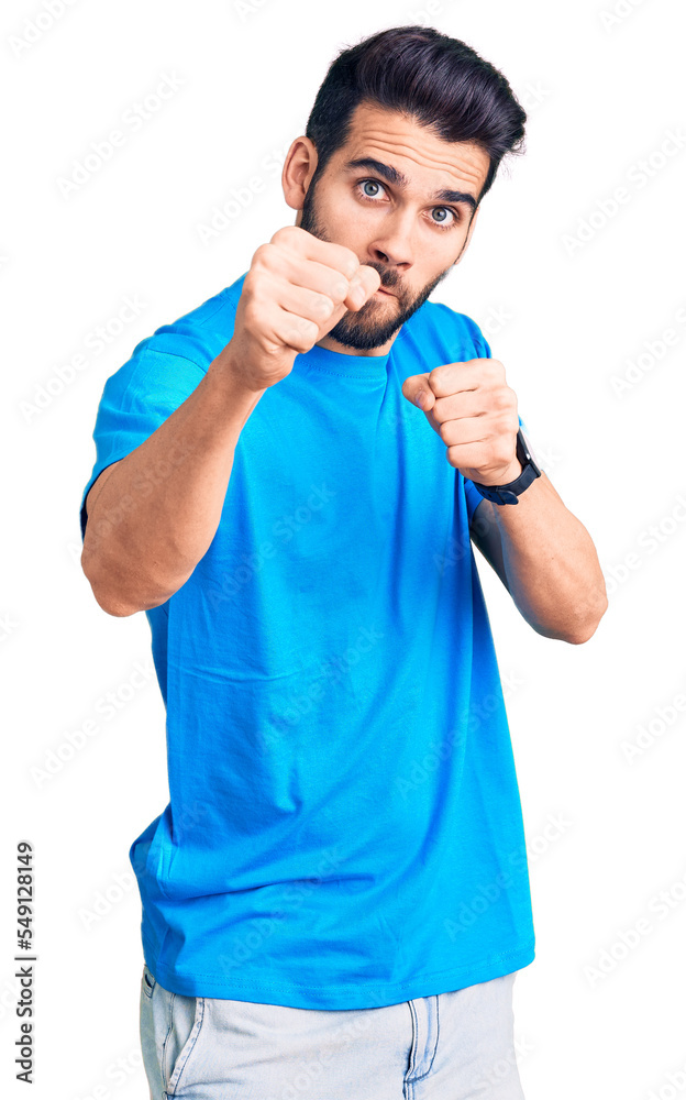 Young handsome man with beard wearing casual t-shirt punching fist to fight, aggressive and angry attack, threat and violence Young handsome man with beard wearing casual t-shirt punching fist to fight, aggressive and angry attack, threat and violence