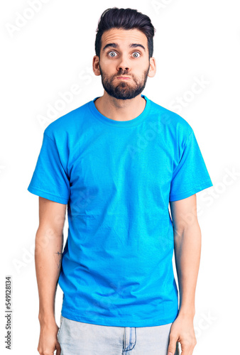 Young handsome man with beard wearing casual t-shirt puffing cheeks with funny face. mouth inflated with air, crazy expression.