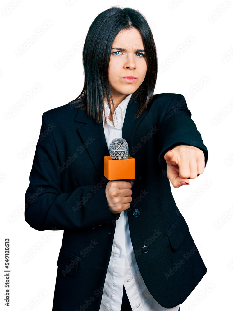 Young brunette woman with blue eyes holding reporter microphone pointing with finger to the camera and to you, confident gesture looking serious