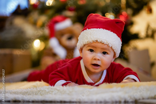 happy laughing baby in christmas outfit or santa claus dress crawling infront of xmas tree on a blanket on the floor in a cozy living room 