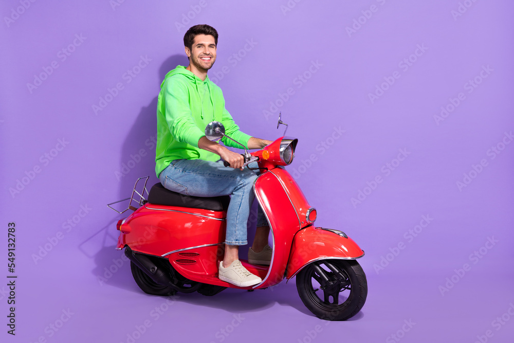 Full size photo of attractive handsome positive guy dressed green hoodie sitting on new motorcycle isolated on violet color background Full size photo of attractive handsome positive guy dressed green hoodie sitting on new motorcycle isolated on violet color background