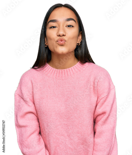 Young asian woman wearing casual winter sweater looking at the camera blowing a kiss on air being lovely and sexy. love expression. © Krakenimages.com