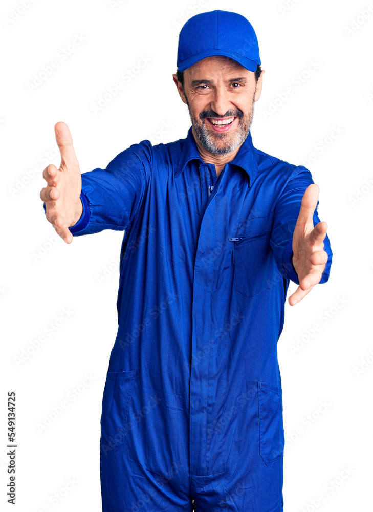 Middle age handsome man wearing mechanic uniform looking at the camera smiling with open arms for hug. cheerful expression embracing happiness.