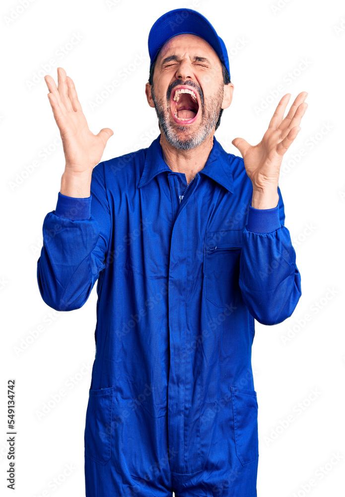 Middle age handsome man wearing mechanic uniform celebrating mad and crazy for success with arms raised and closed eyes screaming excited. winner concept Middle age handsome man wearing mechanic uniform celebrating mad and crazy for success with arms raised and closed eyes screaming excited. winner concept