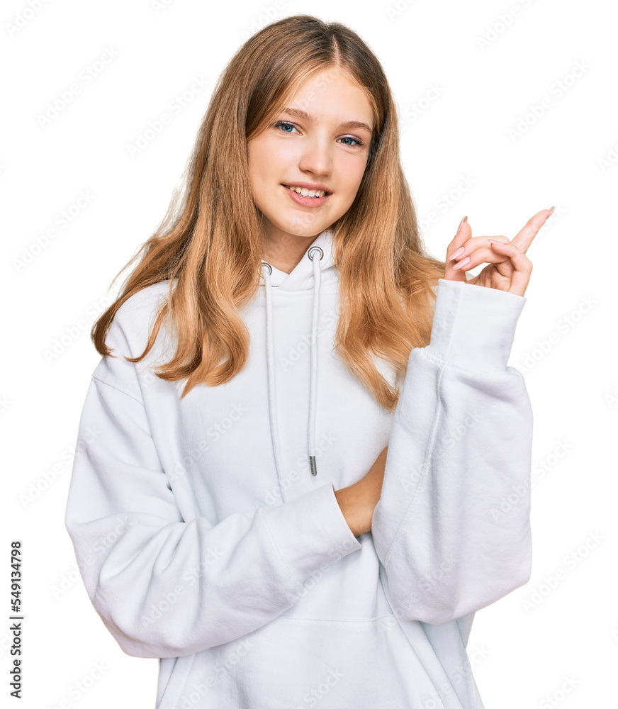 Beautiful young caucasian girl wearing casual sweatshirt with a big smile on face, pointing with hand and finger to the side looking at the camera.