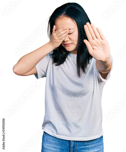Young chinese woman wearing casual white t shirt covering eyes with hands and doing stop gesture with sad and fear expression. embarrassed and negative concept.