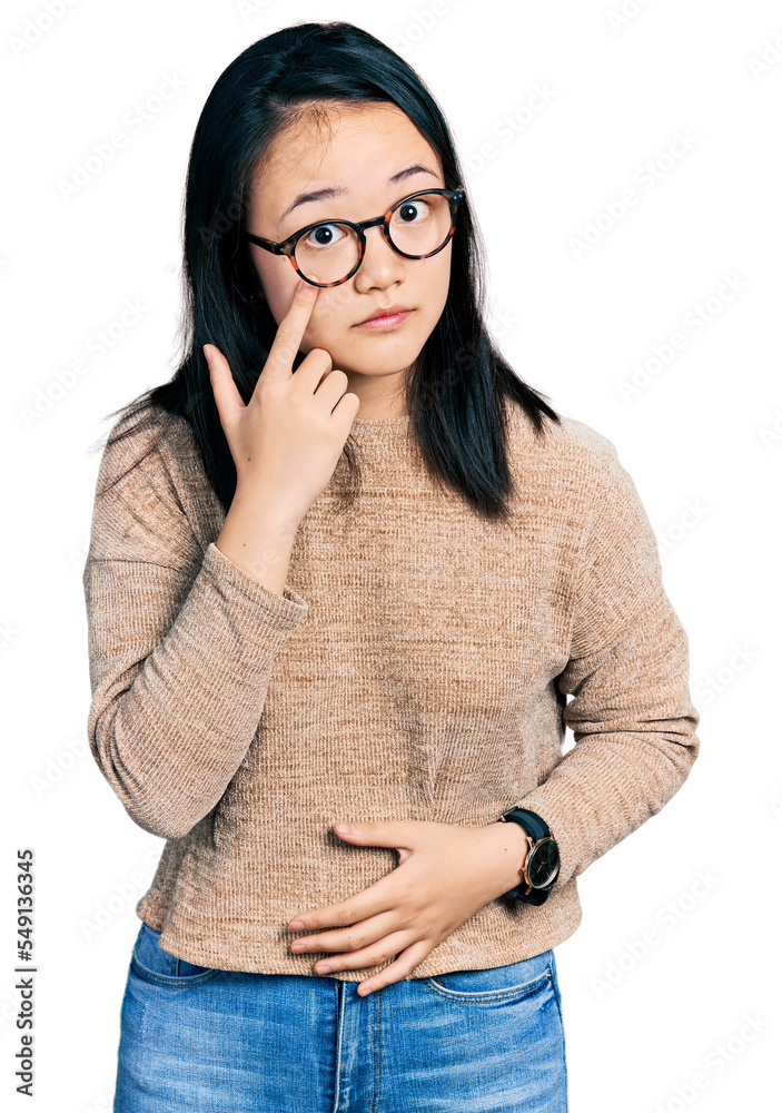 Young chinese woman wearing casual sweater and glasses pointing to the eye watching you gesture, suspicious expression