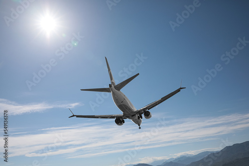 Modern white airplane flying in sky near mountains