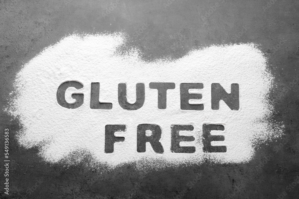 Fototapeta premium Words Gluten free written with flour on grey background, top view