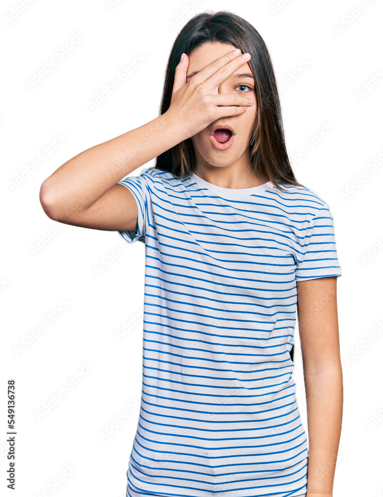 Young brunette girl with long hair wearing casual striped t shirt peeking in shock covering face and eyes with hand, looking through fingers afraid Young brunette girl with long hair wearing casual striped t shirt peeking in shock covering face and eyes with hand, looking through fingers afraid
