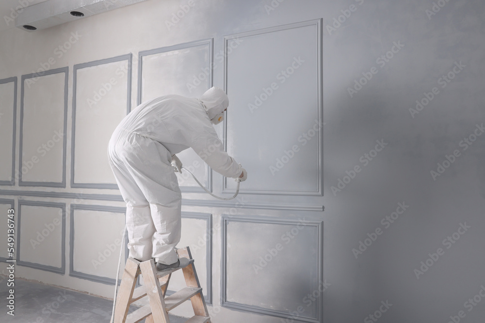 Decorator dyeing wall in grey color with spray paint