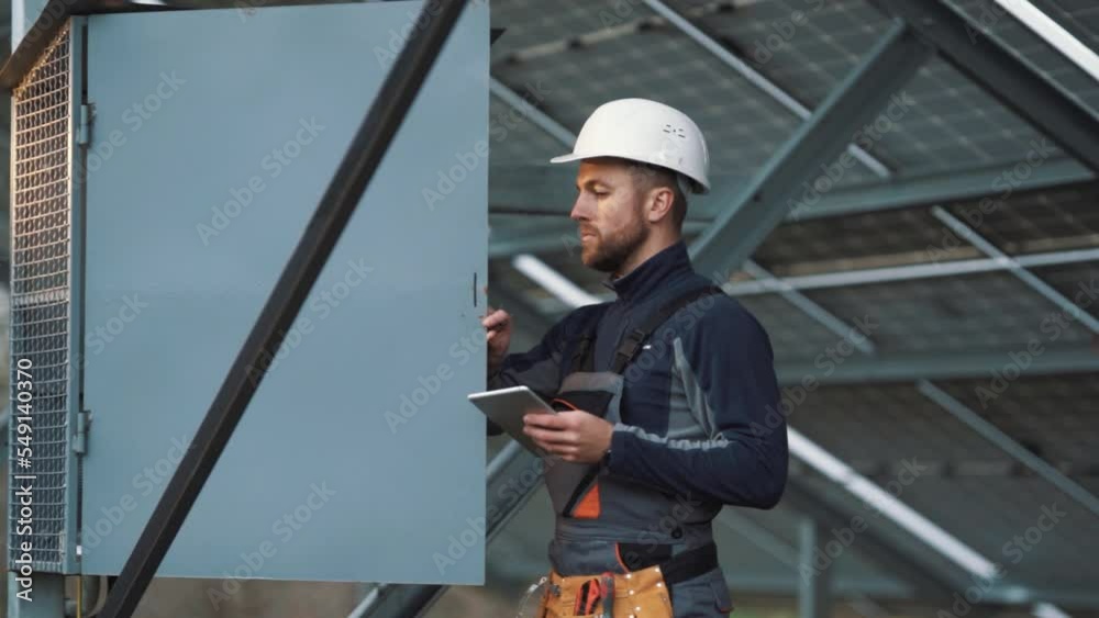 A professional man in a special electrician's uniform opens the switchboard and conducts a technical inspection with a tablet A professional man in a special electrician's uniform opens the switchboard and conducts a technical inspection with a tablet