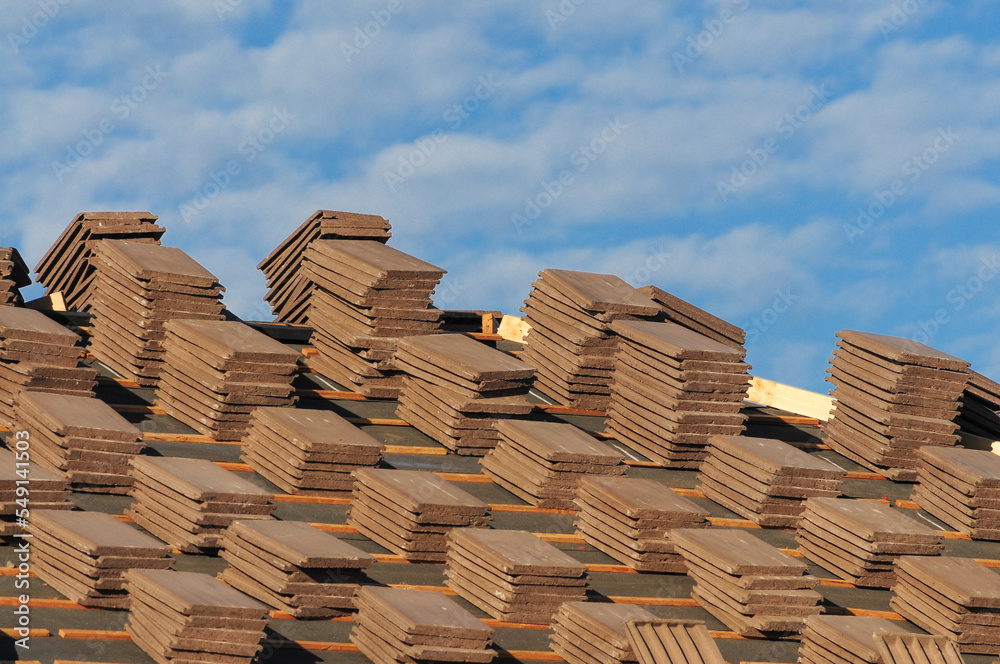 Fototapeta premium Stacks of concrete roof tiles staged on underlayment during residential construction, prepared for installation as part of roofing system on a new home build