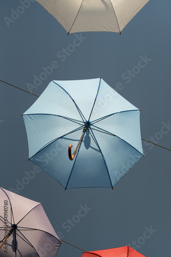 Fotografie, Obraz Colorful umbrellas fixed on steel ropes between buildings against blue sky