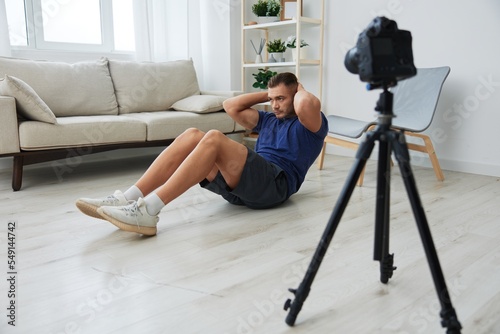 Fotografie, Obraz Man athlete blogger records exercise training on the body at home on camera, spo