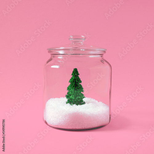 Christmas tree with snow in a glass jar on pastel pink background. Creative winter background. Flat lay, top view.