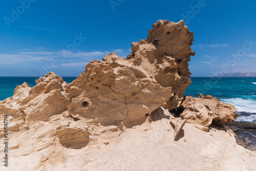 Huge light beige colored rock formation with gaps and turquoise ocean in distance, Fuerteventura 