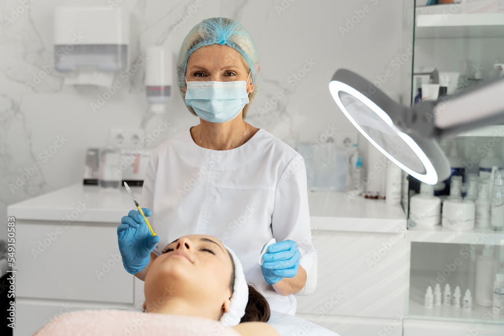 Cosmetologist looking to the camera while doing injections for lips augmentation Cosmetologist looking to the camera while doing injections for lips augmentation