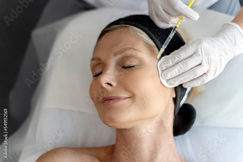 Senior woman relaxing during facial mesotherapy for smoothing of mimic wrinkles