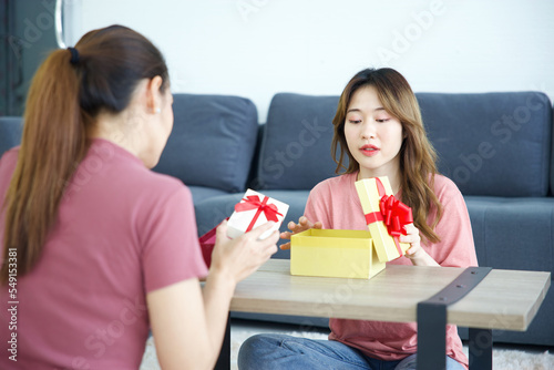 young woman smiling and opening a gift box with her friend on a table