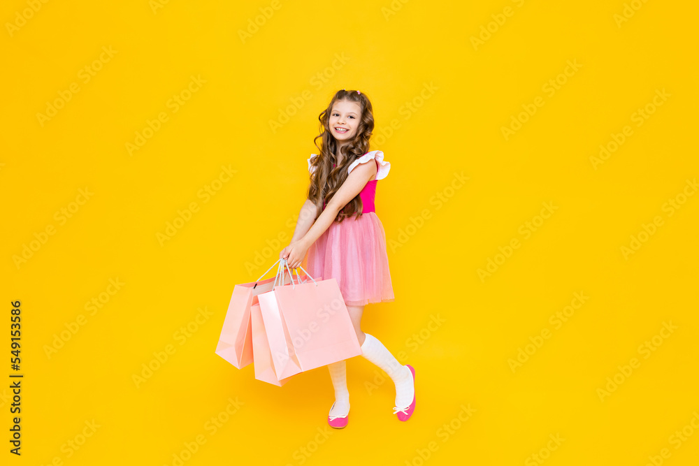 A little girl with full-length shopping. A fashionista after shopping on a yellow isolated background. Children's sale. The young princess is happy to make new purchases. A little girl with full-length shopping. A fashionista after shopping on a yellow isolated background. Children's sale. The young princess is happy to make new purchases.