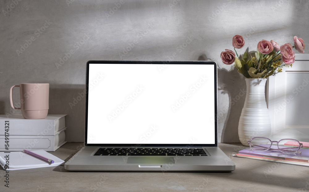 Fototapeta premium Feminine workspace with laptop, books, coffee cup and pink rose in vase. Blank screen for your advertise text.