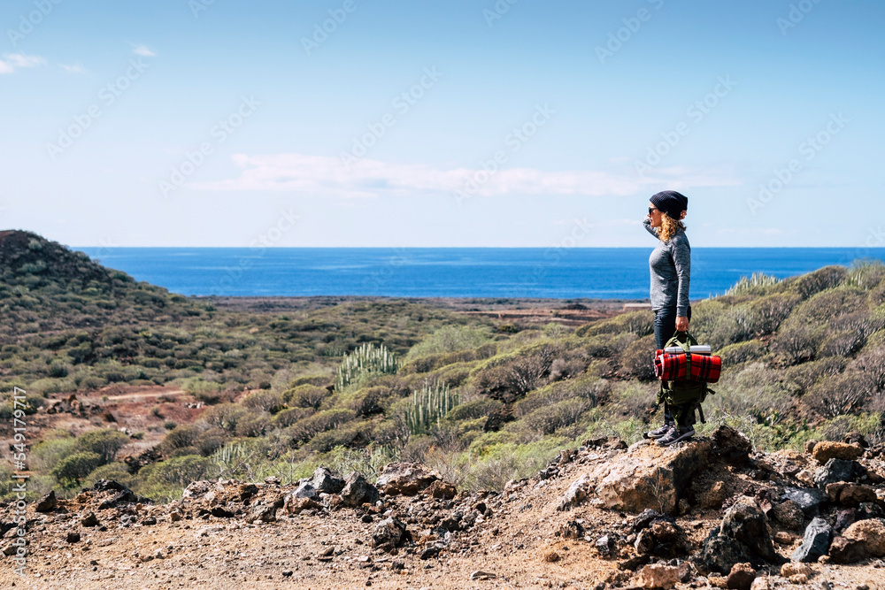 One standing woman enjoying and admiring panorama landscape in outdoor leisure activity after hiking trekking walk. Ocean and sea view with blue sky at the horizon. Travel and adventure lifestyle