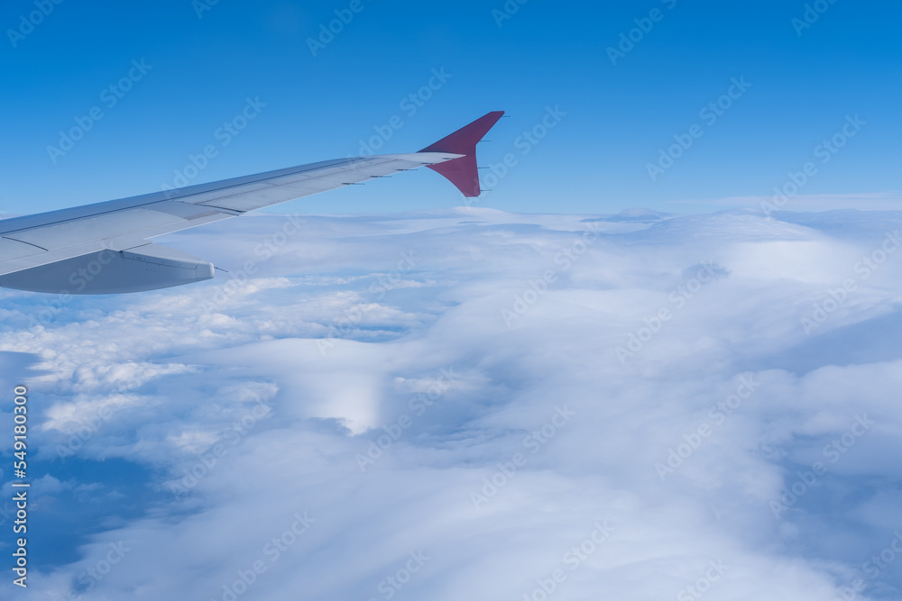 Fototapeta premium The view from the window of the plane on the wing of the plane against the background of fluffy curly clouds and blue sky. The concept of travel.