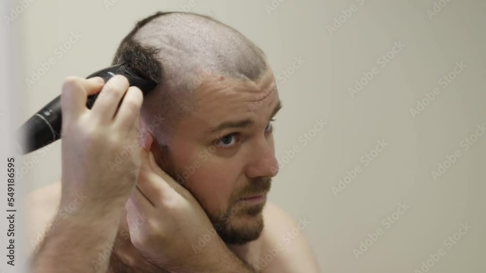 man cuts his head with a clipper in front of a mirror man cuts his head with a clipper in front of a mirror